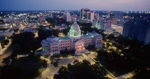 A large, historic building with a central dome and multiple wings, surrounded by a well-maintained park and modern buildings in the background. - Hilton Jackson (Jackson)