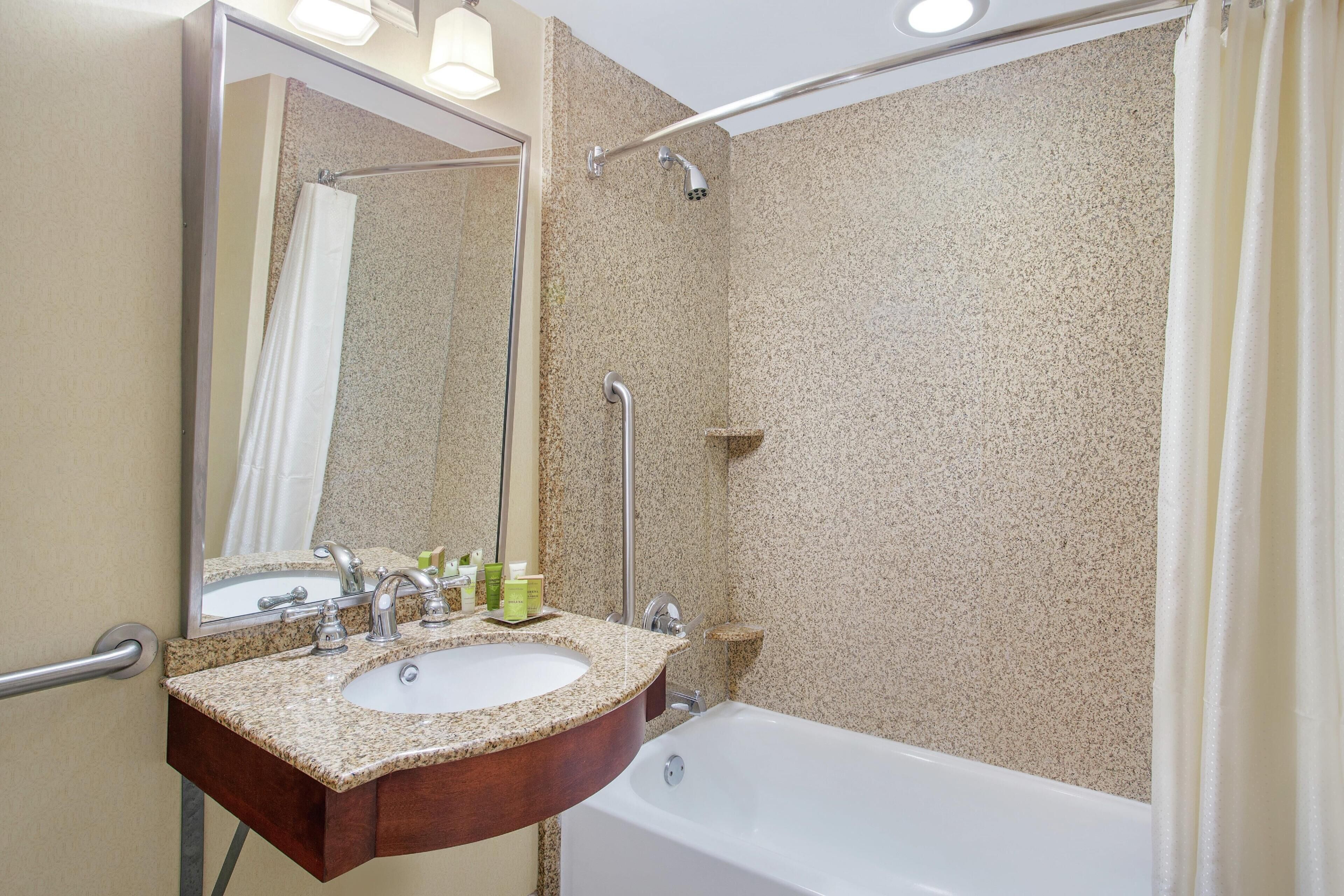 A bathroom with a granite countertop sink, a mirror, a shower, and a bathtub.