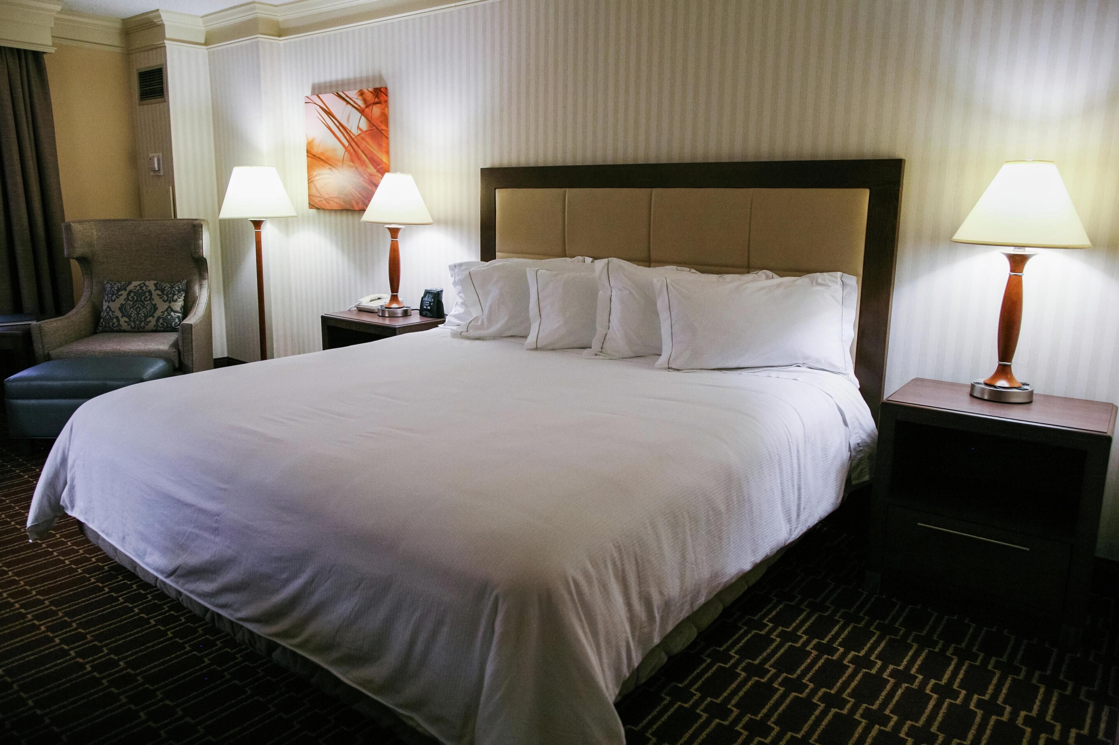 A hotel room with a large bed, two bedside tables with lamps, a chair, and a wall-mounted artwork.