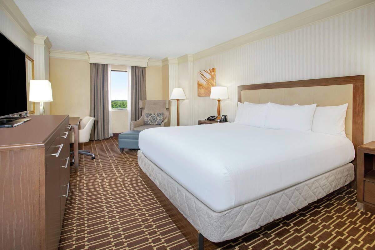A hotel room with a large bed, a desk, a chair, a TV, and a window with curtains.