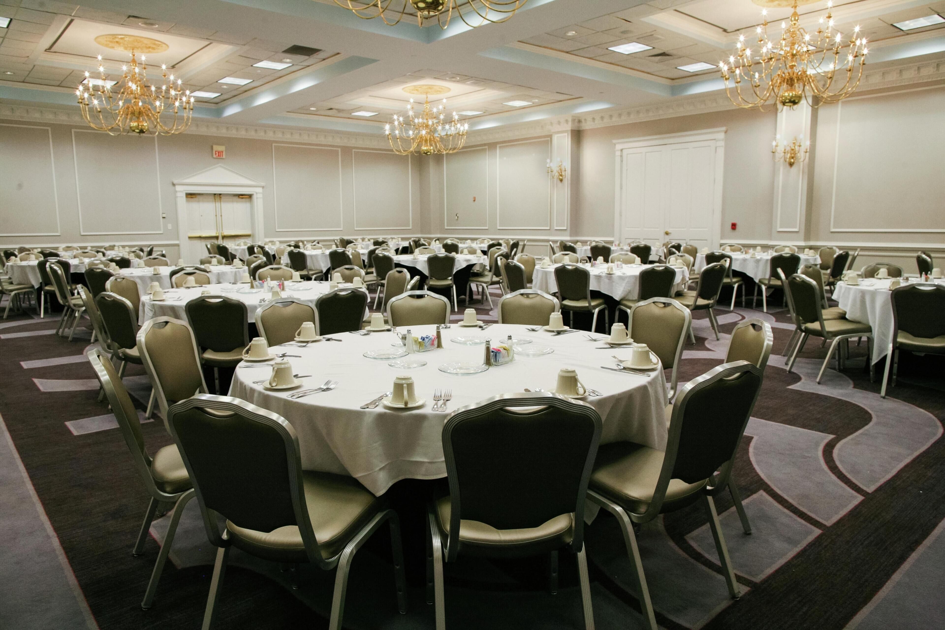Une grande salle de conférence équipée de tables rondes, de chaises et de lustres.