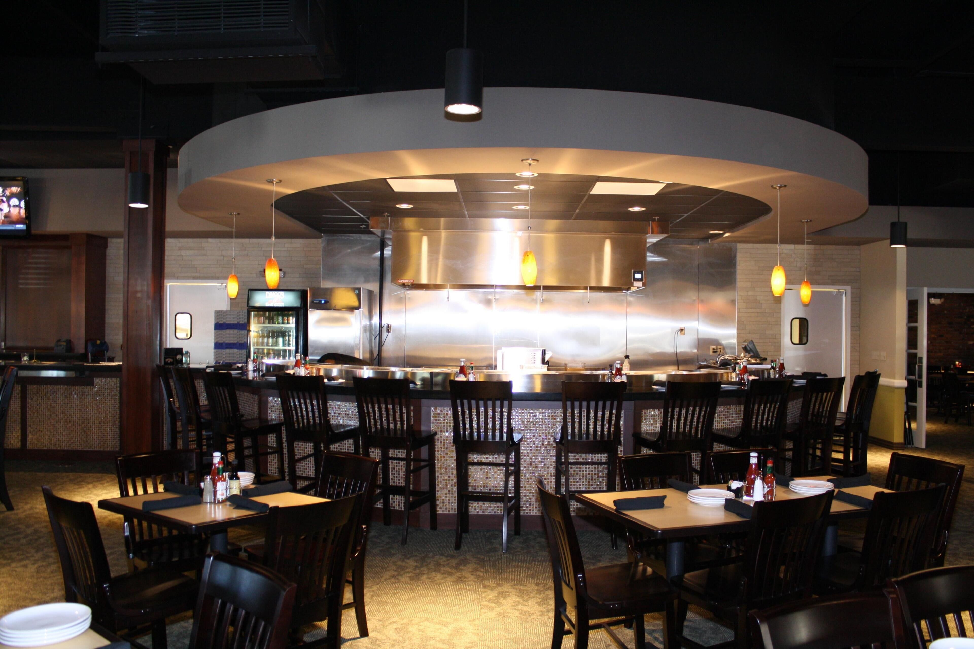A restaurant with a curved bar, multiple seating areas, and a kitchen in the background.