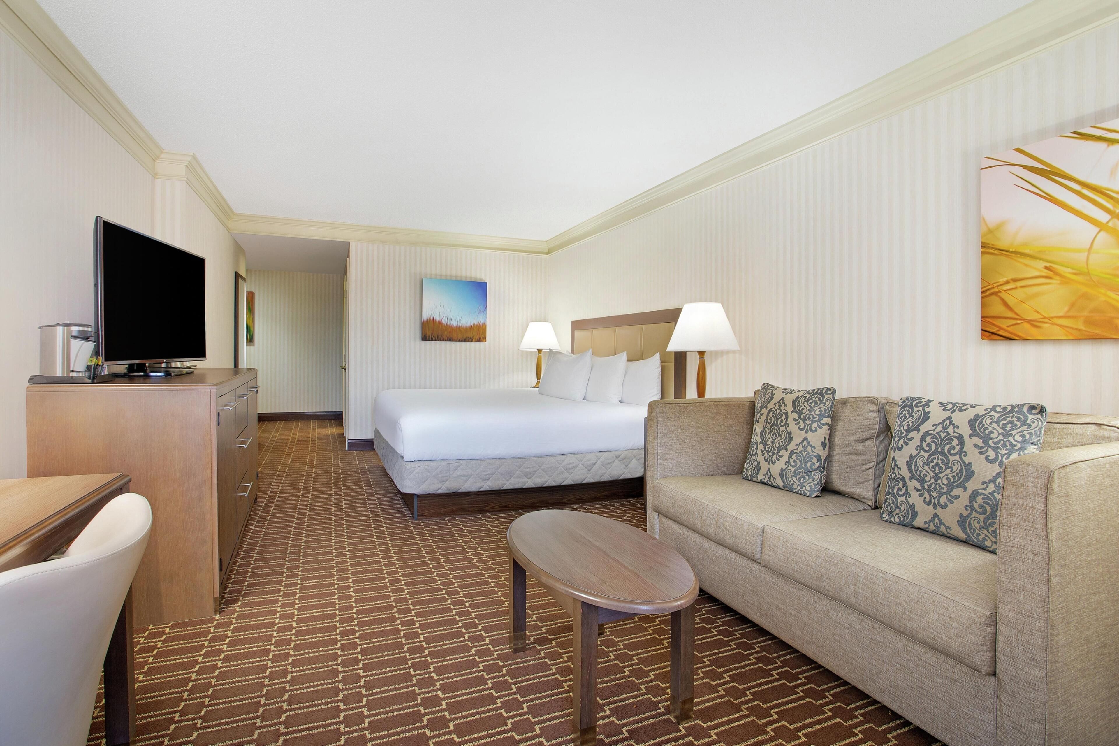 A hotel room with a bed, a sofa, a TV, a desk, and a painting on the wall.