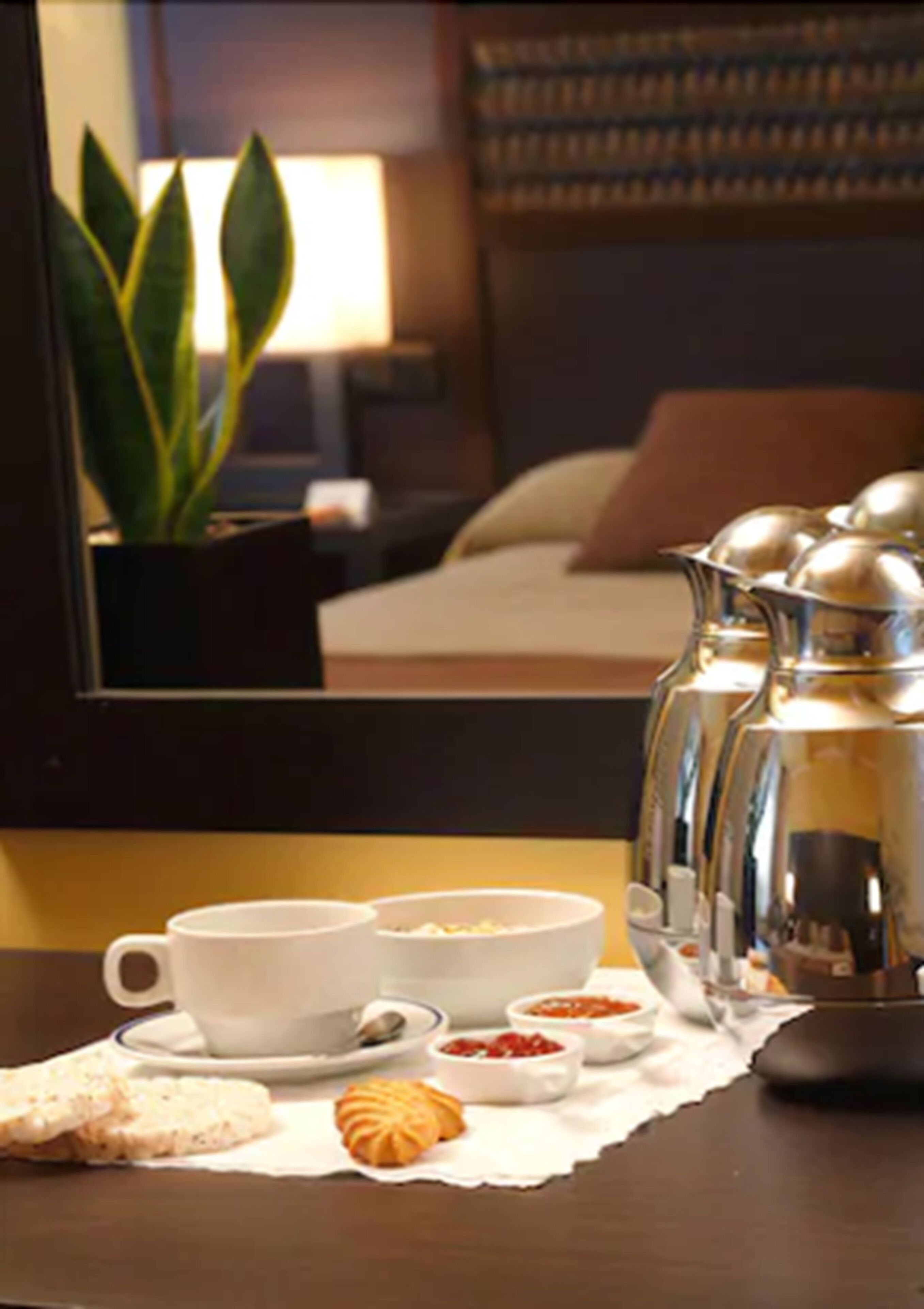 Una habitación de hotel con cama, una mesita de noche con cafetera, tazas y bollería.