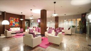 A modern lobby with white sofas, a colorful abstract art piece on the wall, and a marble floor. - Hotel Spa Congreso (Teo)