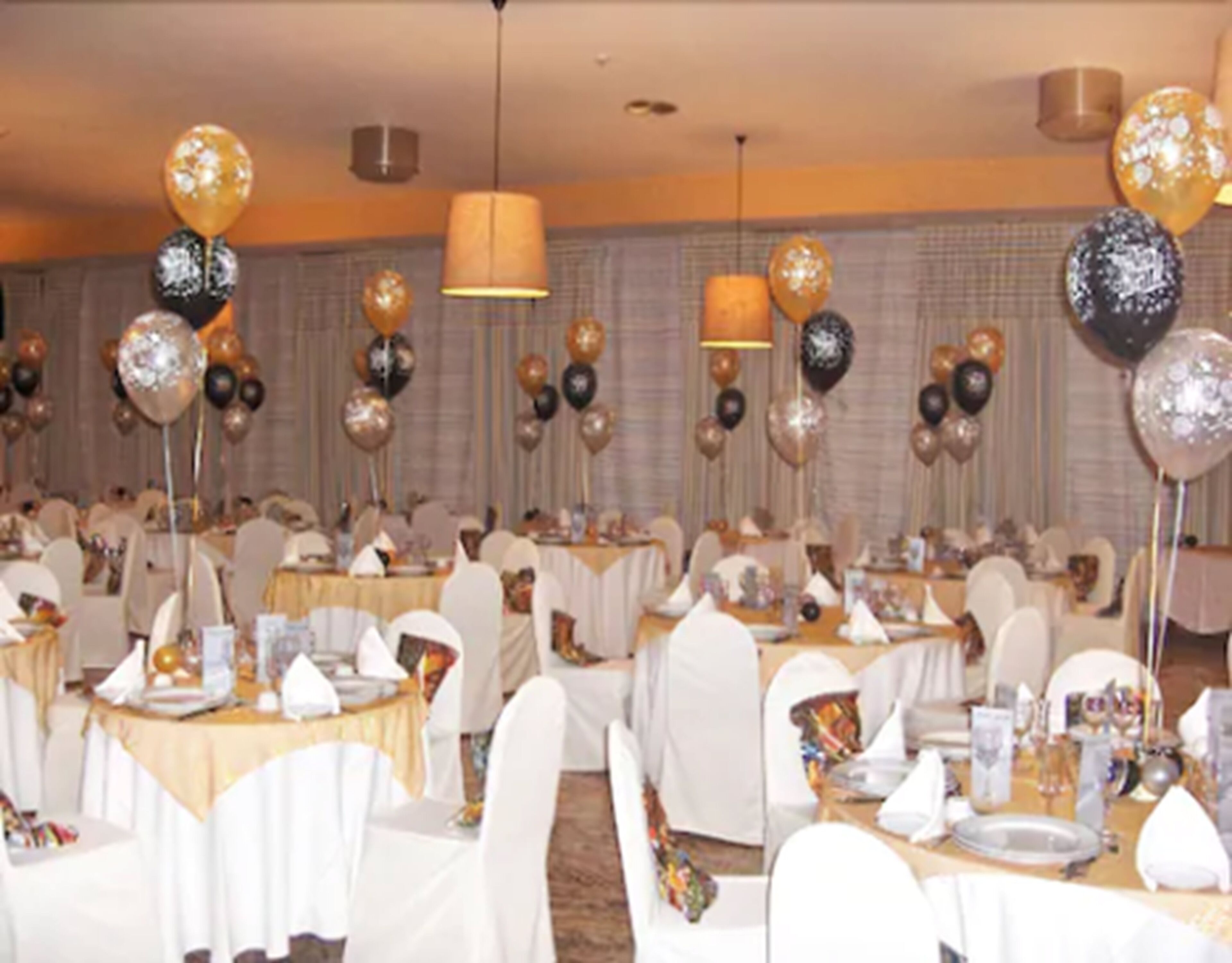 A banquet hall with round tables covered in white tablecloths, surrounded by white chairs.
