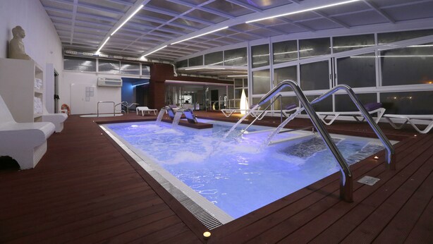 A hot tub area with a wooden deck, metal railings, and a statue. - Hotel Spa Congreso (Teo)