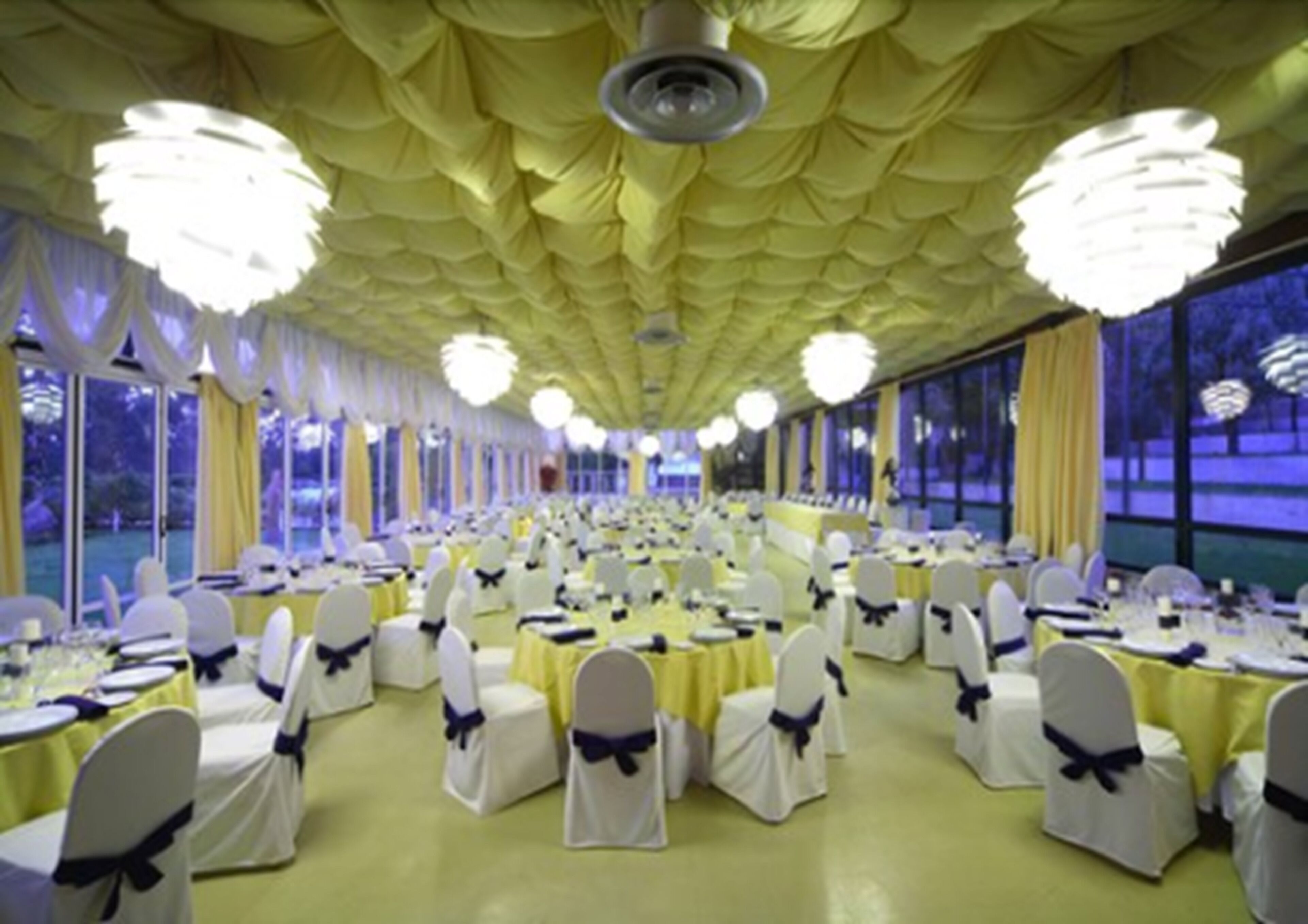 A banquet hall with rows of tables, each with white chairs tied with blue sashes.