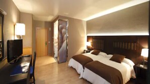 A hotel room with a bed, a desk with a computer, a mirror, and a door leading to another room. - Hotel Spa Congreso (Teo)