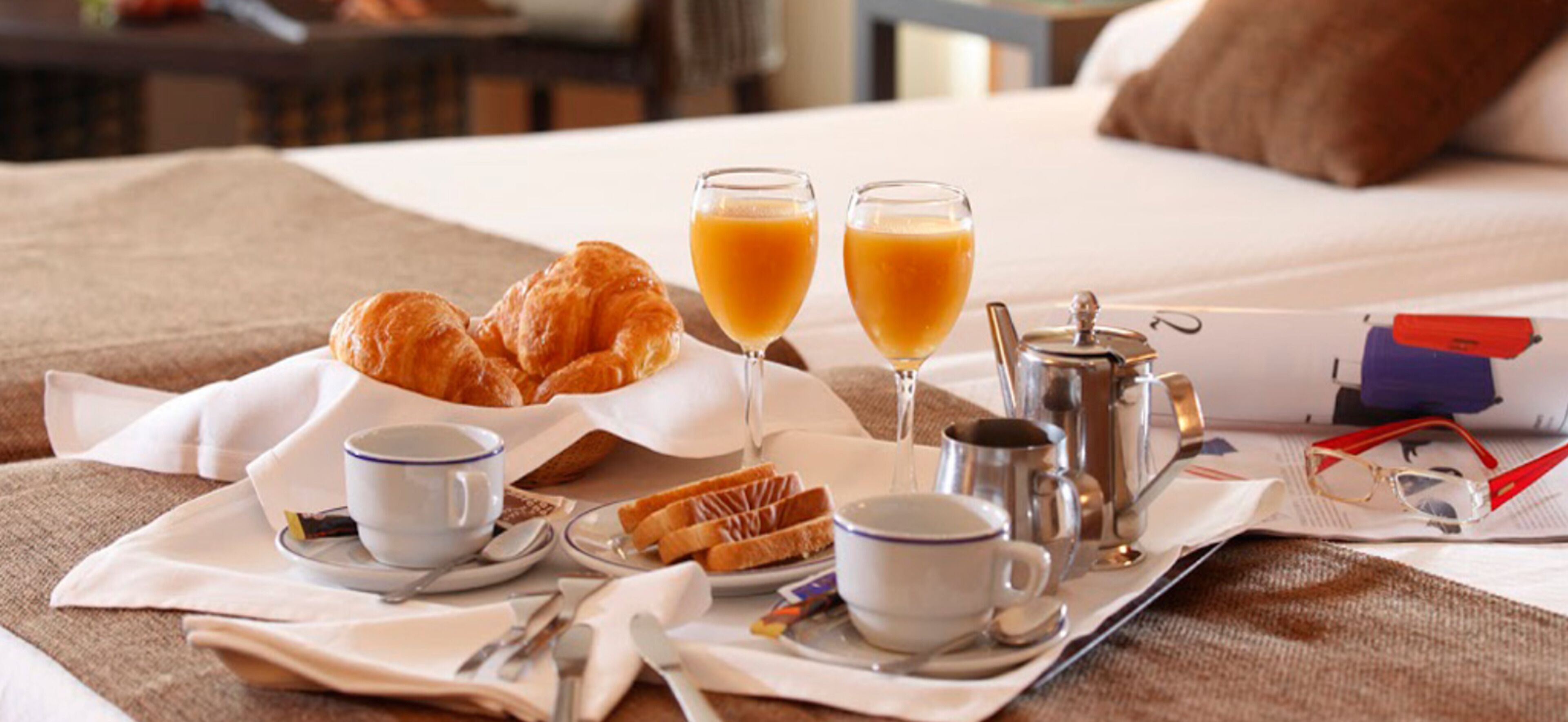 Esmorzar preparat sobre el llit, amb croissants, suc d'aranja, cafè i una teiera.