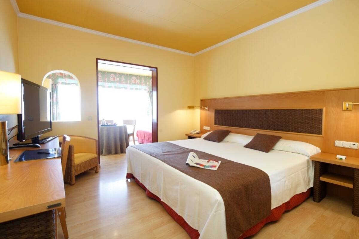 Une chambre d’hôtel avec un lit, des tables de chevet, une télévision et une fenêtre avec des rideaux.