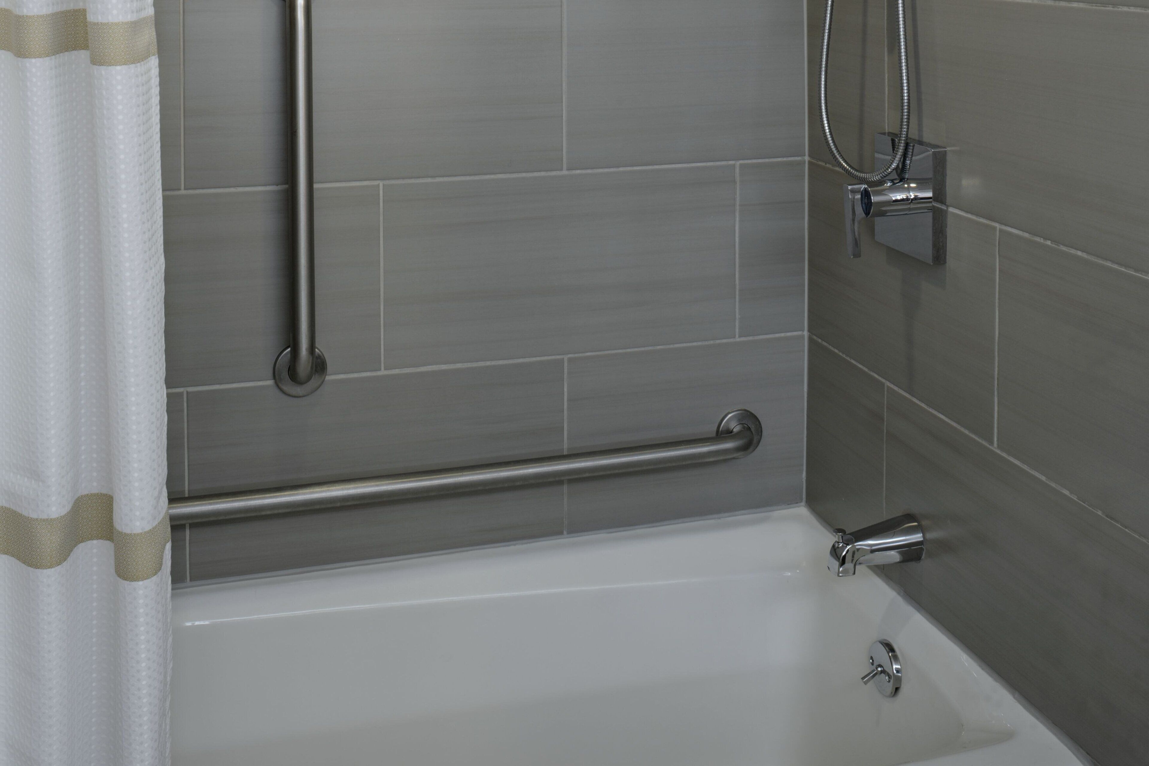 Un baño con bañera, barras de apoyo y cabezal de ducha.