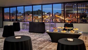 A room with large windows, a bar area with bottles, and a buffet table with food. - Marriott East Lansing at University Place (East Lansing)