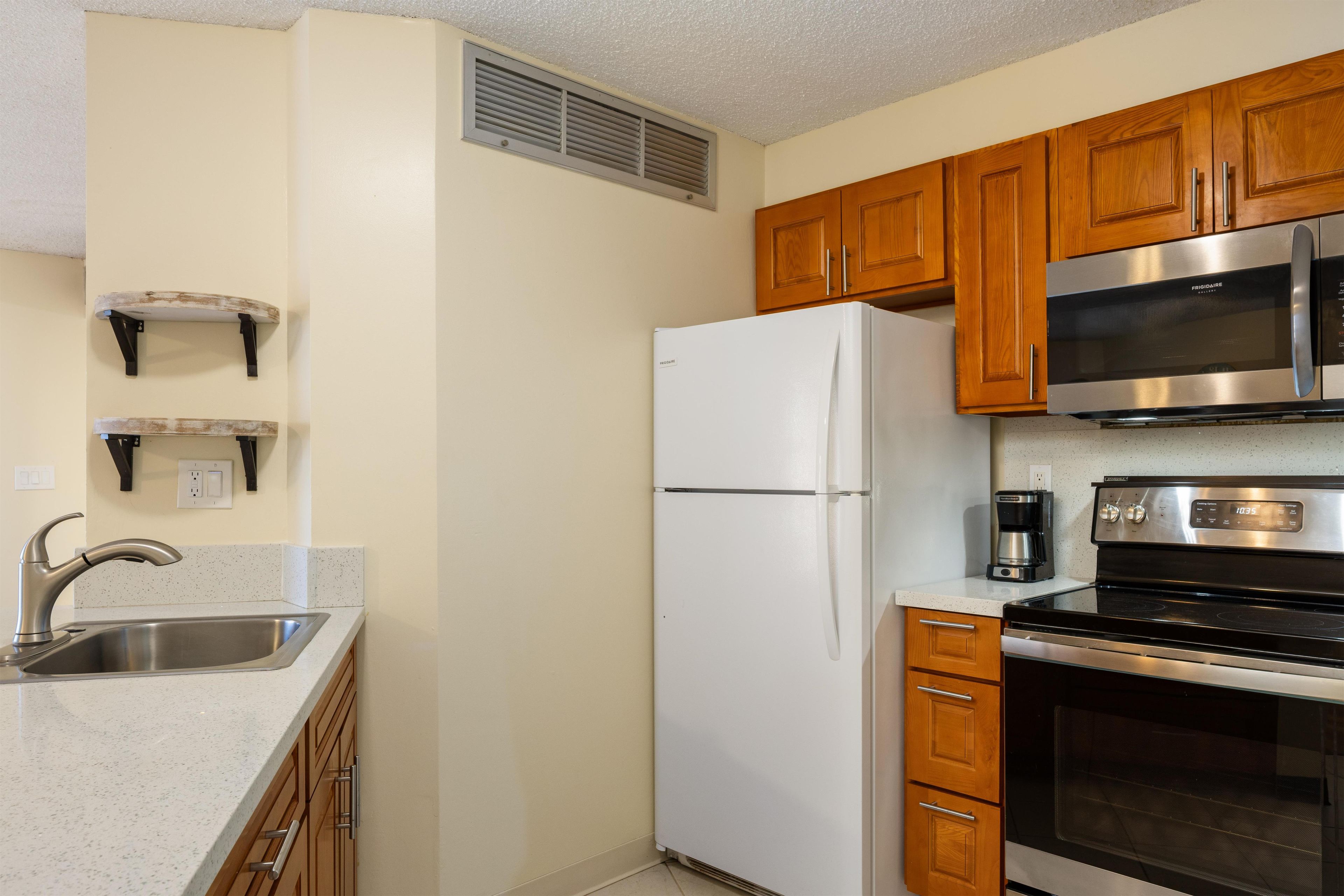 A kitchen with wooden cabinets, a stainless steel refrigerator, a microwave, a coffee maker, and a stove.