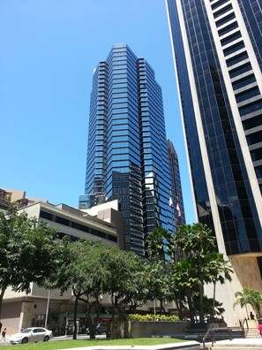 A tall, modern building with a glass facade and a prominent American flag. - Aston at the Executive Centre Hotel (Honolulu)
