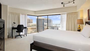 A hotel room with a large bed, a desk, a chair, and a view of the cityscape through the window.