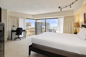 A hotel room with a large bed, a desk, a chair, and a view of the cityscape through the window.