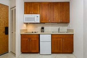 Una cocina compacta con armarios de madera, un microondas blanco, una cafetera y un refrigerador.