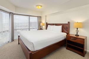 A hotel room with a large bed, two bedside tables with lamps, a view of the city through the window, and a carpeted floor.