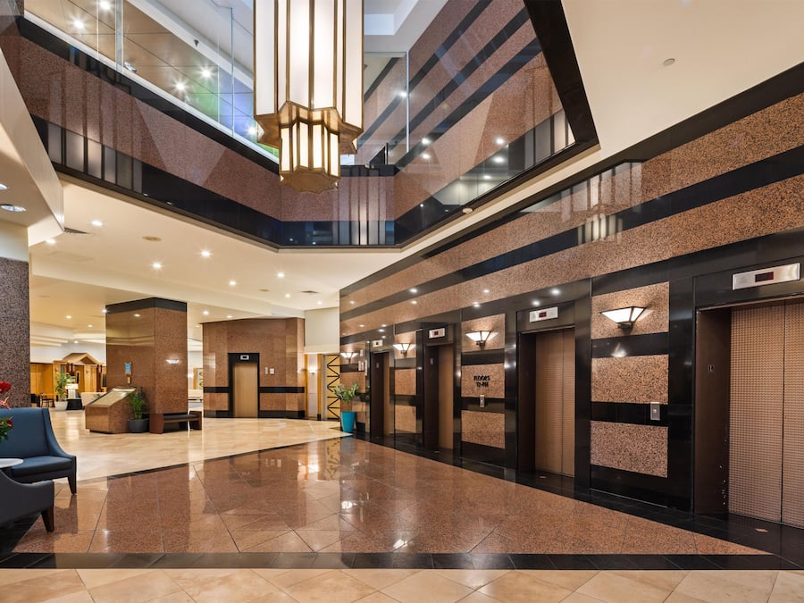 A modern hotel lobby with a polished floor, a reception desk, seating area, and multiple elevators.