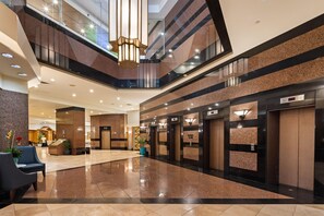 A modern hotel lobby with a polished floor, a reception desk, seating area, and multiple elevators. - Aston at the Executive Centre Hotel (Honolulu)
