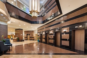 A modern hotel lobby with a polished floor, a reception desk, seating area, and multiple elevators.