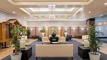 A hotel lobby with a central seating area, multiple tables, and potted plants.
