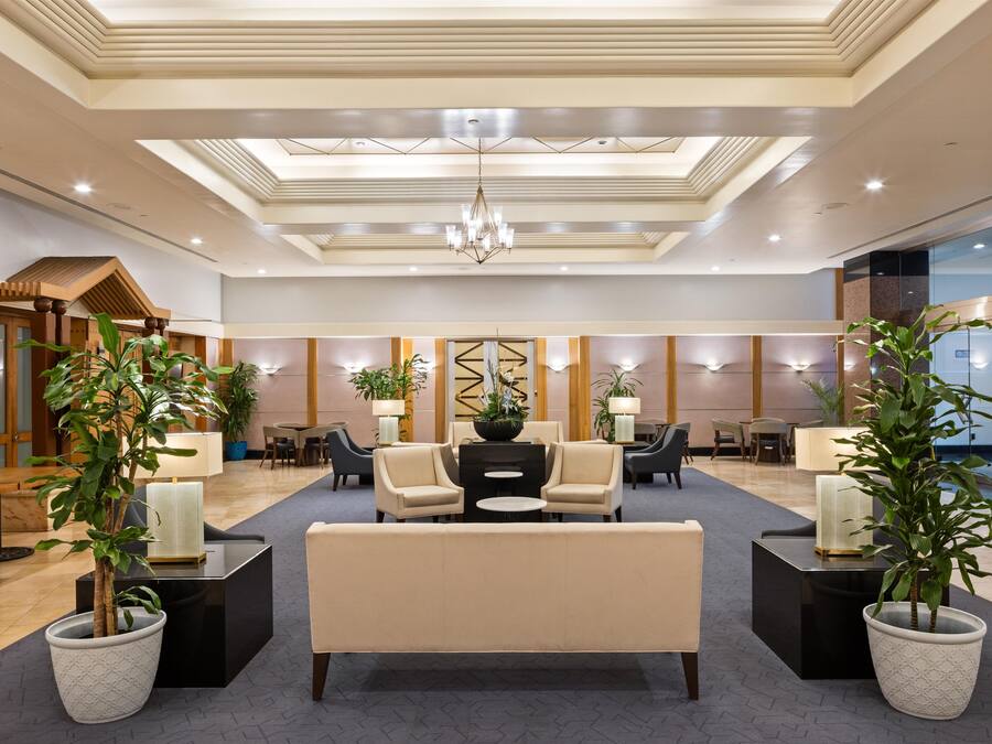 A hotel lobby with a central seating area, multiple tables, and potted plants.
