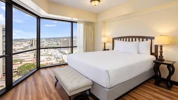 A hotel room with a large bed, a bench, a nightstand, and a view of the city.