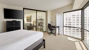 Habitación de hotel con cama, escritorio, silla, armario, televisor y una ventana grande con vista a la ciudad.