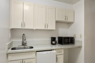 Una cocina compacta con armarios blancos, un lavamanos de acero inoxidable, una cafetera, un microondas y un lavavajillas.