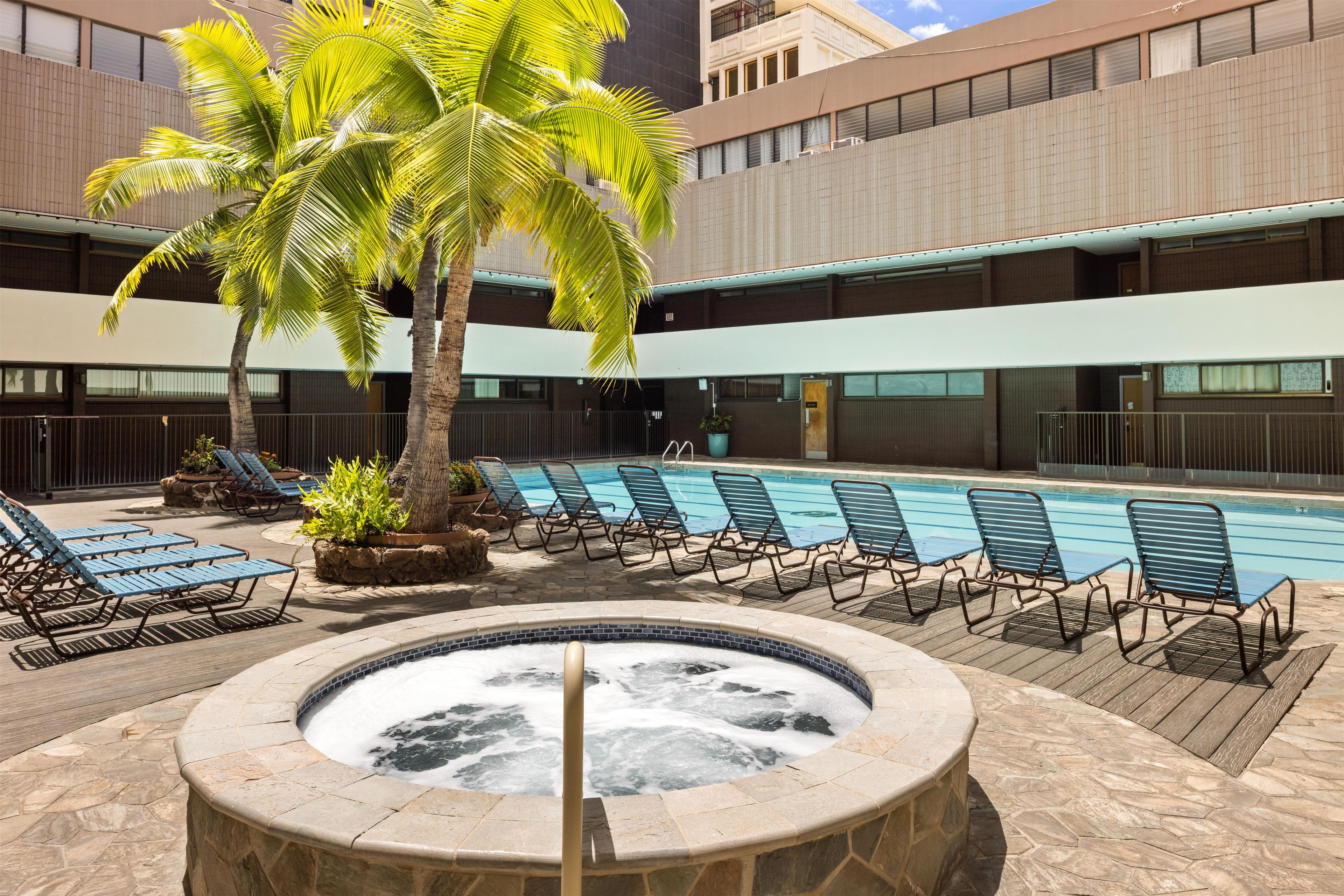Un área de piscina con sillas de descanso, un jacuzzi y palmeras.