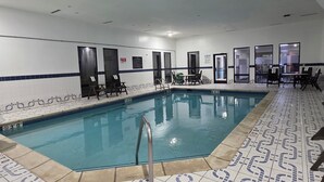 A swimming pool with a tiled floor and walls, surrounded by chairs and tables. - Sonesta Essential Ames (Ames)