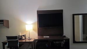 A hotel room with a desk, chair, TV, lamp, and a mirror. - Sonesta Essential Ames (Ames)