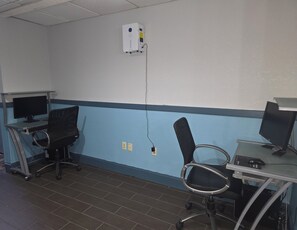 A room with two desks, each with a computer monitor and keyboard, and two black office chairs. There is a whiteboard on the wall and a power outlet near the center. - Sonesta Essential Ames (Ames)