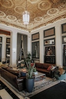 Un'ampia hall con soffitto alto e decorato, divani in pelle, un tavolino da caffè e un'ampia pianta in vaso.