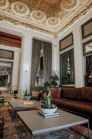 Un salón espacioso con un techo alto y decorativo, un sofá de cuero marrón, una mesa de centro con una planta y una estantería.