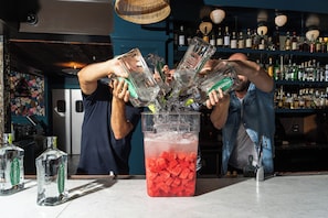 A bar setting with a large pitcher filled with a red drink, surrounded by multiple bottles of liquor and a bar counter. - Sentinel Hotel (Portland)
