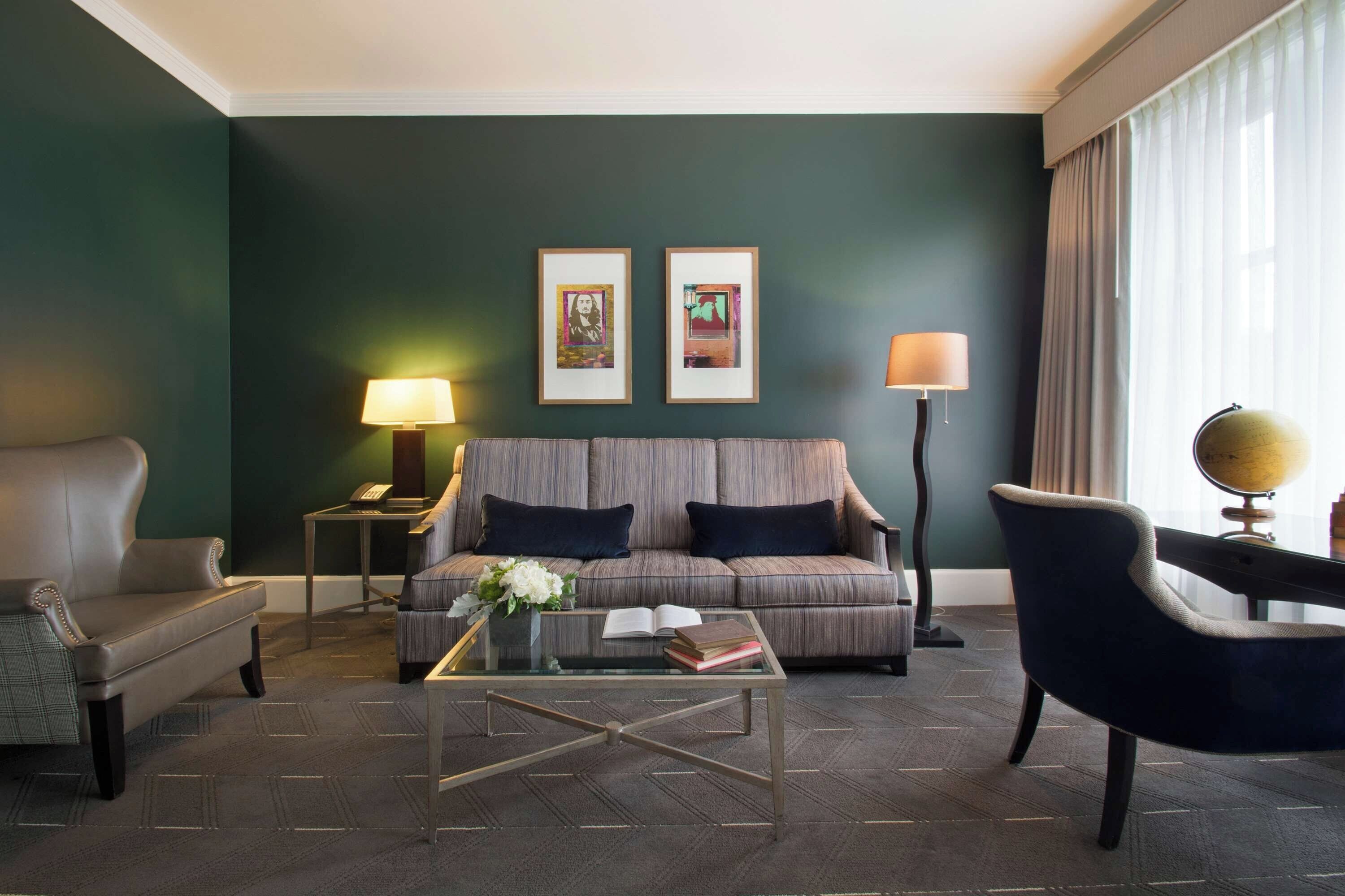 A modern living room with a dark green wall, a sofa, a chair, a coffee table, and two lamps.