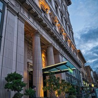 Un edificio classico con ampie colonne, un ingresso in vetro e una segnaletica che indica un hotel.