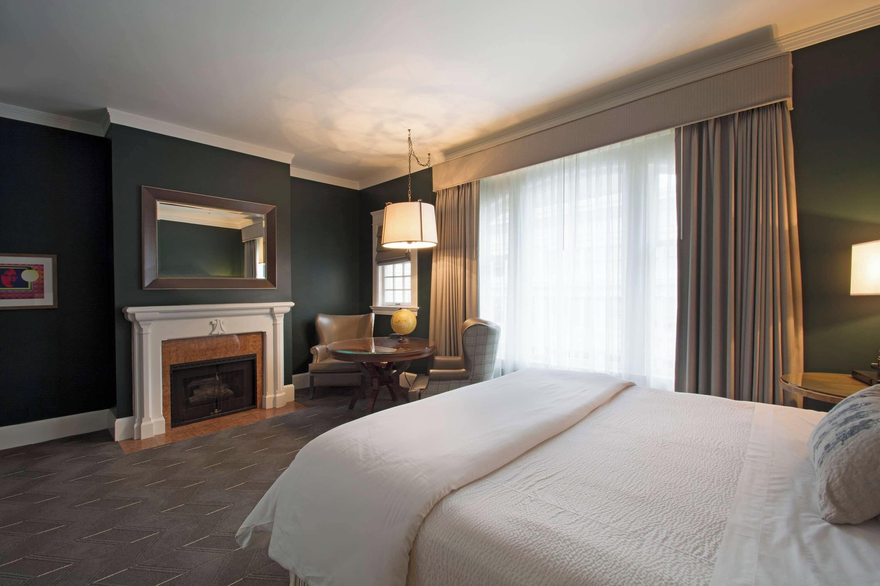 Une chambre d’hôtel avec un grand lit, une cheminée, une table ronde et une chaise.
