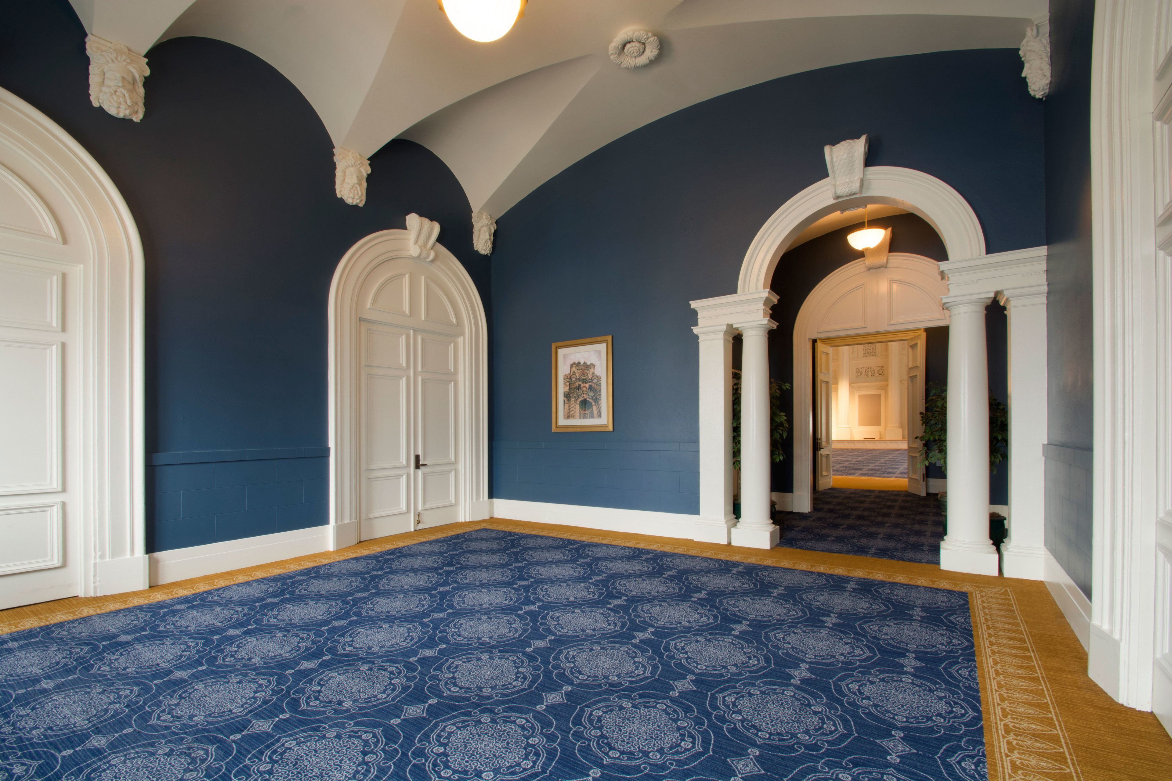 A hallway with blue walls, white doors, and a patterned carpet.