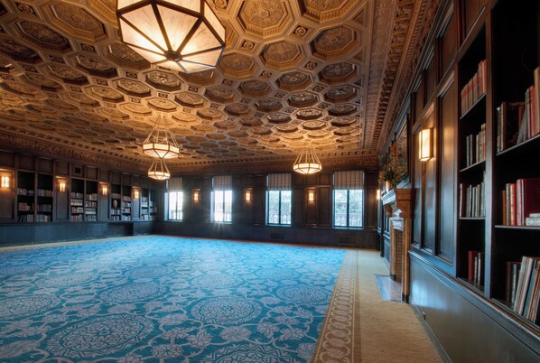 Una habitación amplia con alfombra estampada, techo decorado y estanterías llenas de libros.