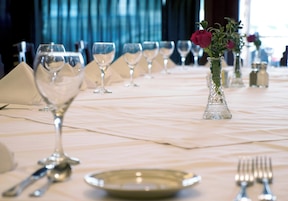 Une table mise pour le dîner, avec des verres à vin, un vase contenant une fleur, et des salières et poivrières.