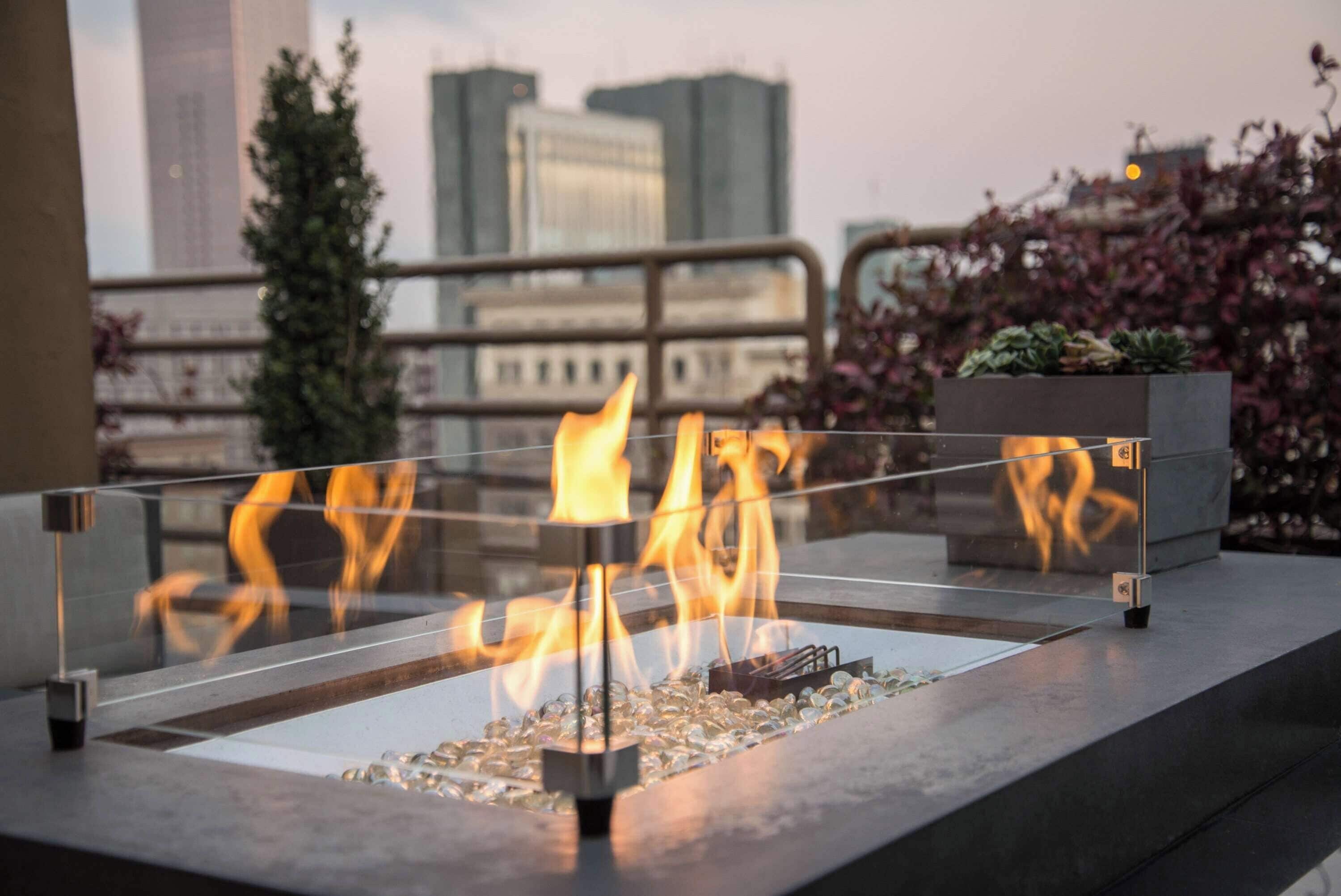 A fire feature with a glass enclosure, surrounded by a metal railing, with a cityscape view in the background.