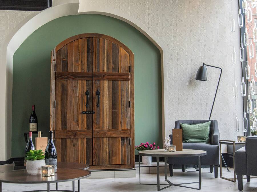 A room with a large wooden door, a round table with a candle, and a chair with a cushion.
