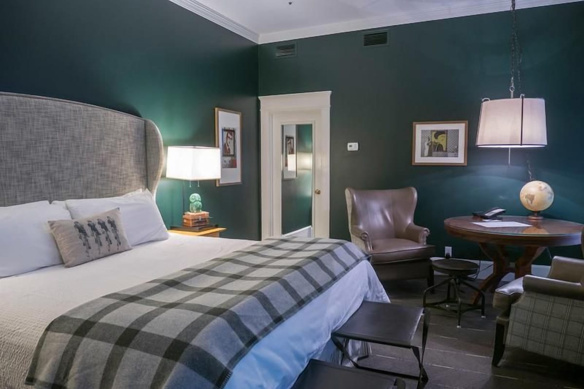 Una habitación de hotel con una cama grande, una silla, una mesita y una lámpara.