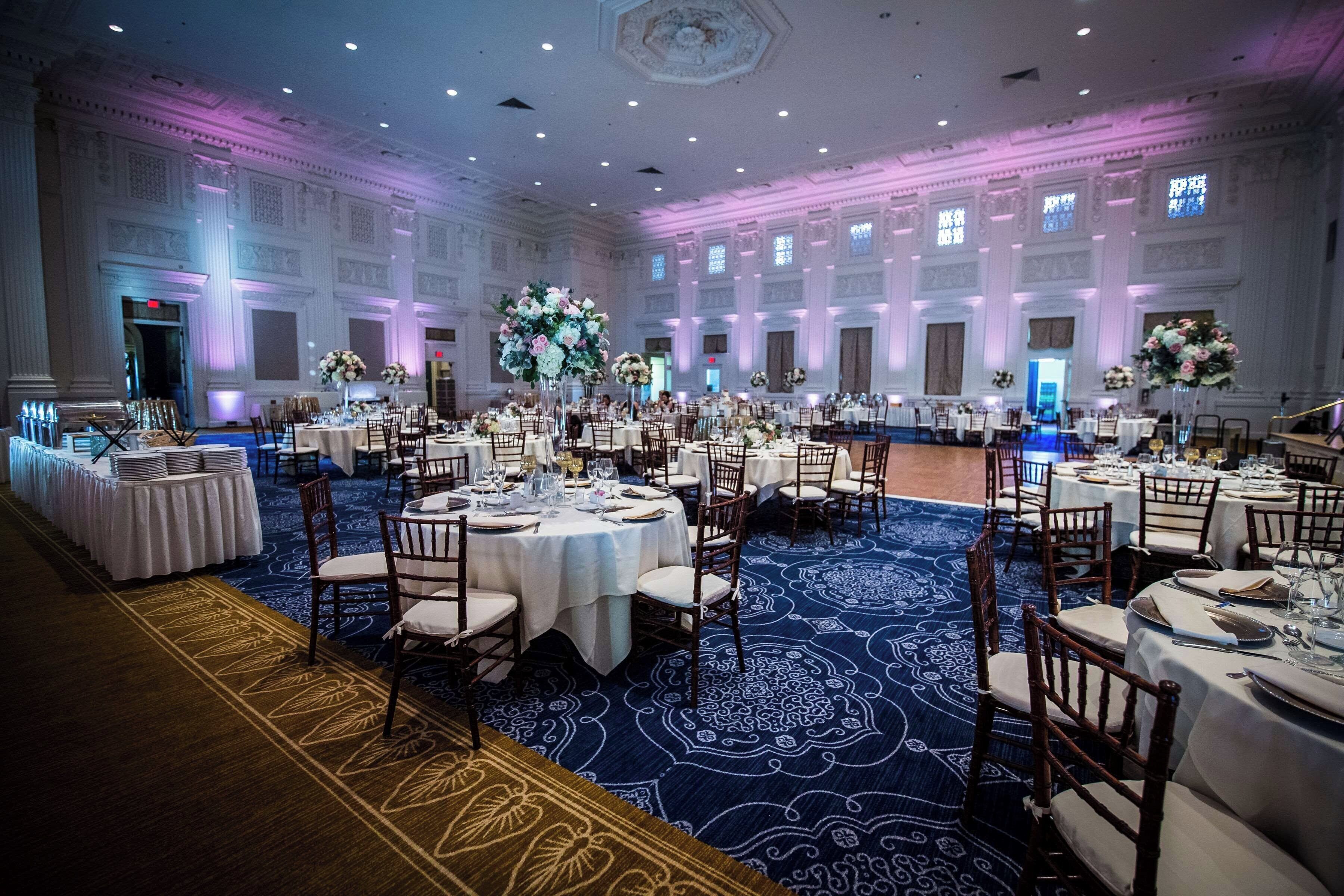A banquet hall with round tables, chairs, and floral centerpieces.