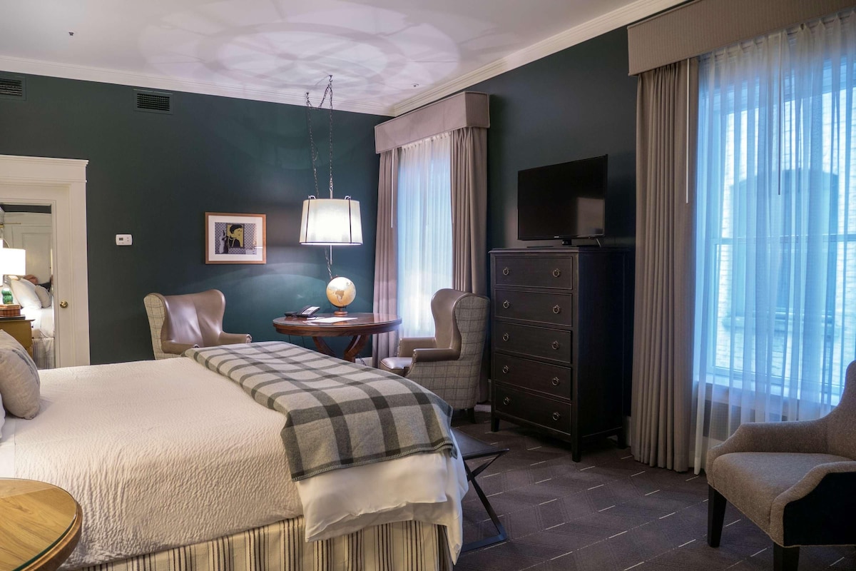 A hotel room with a bed, a desk, a chair, a dresser, a television, and a window with curtains.