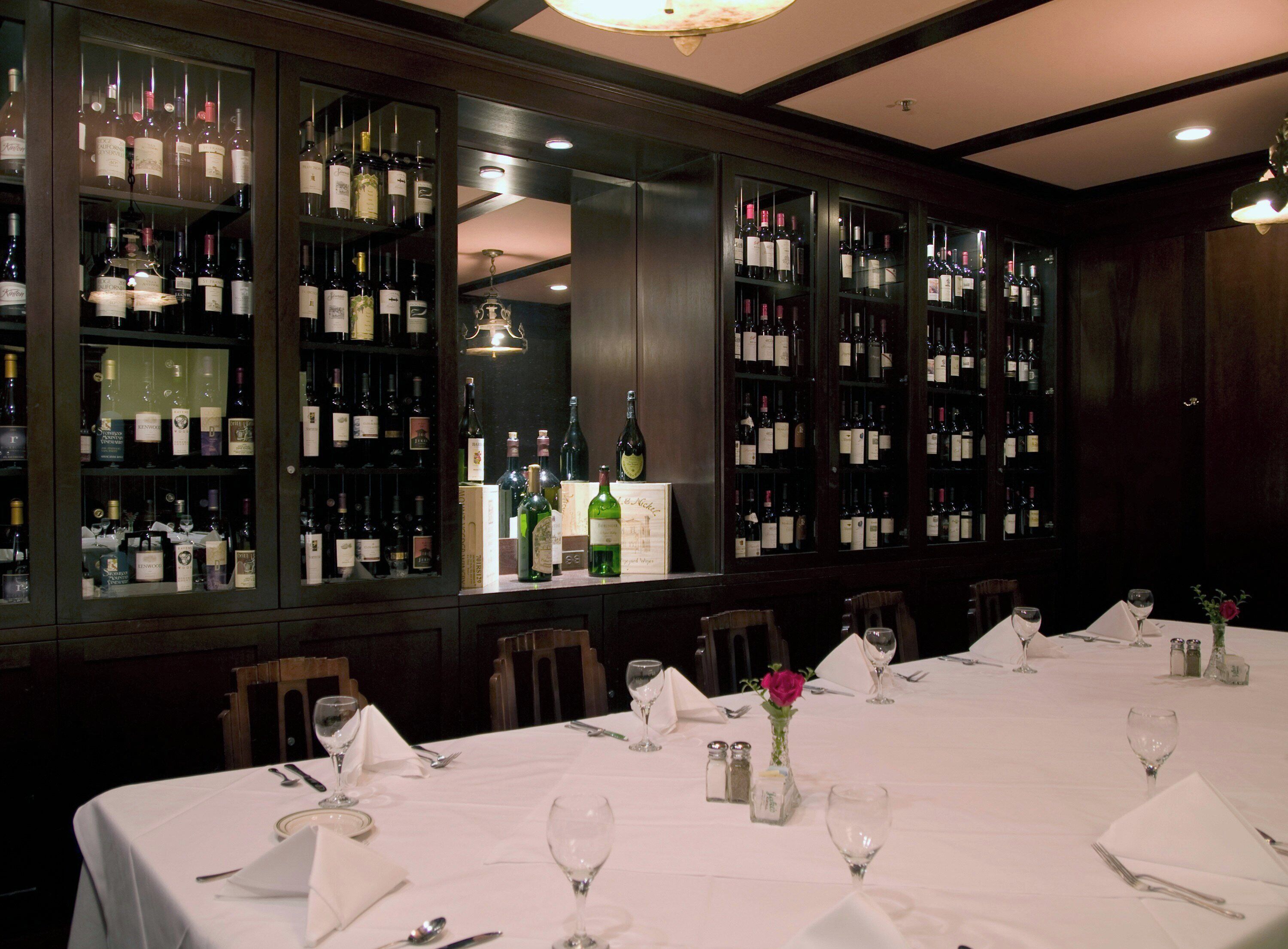 A restaurant with a long table set for dining, wine bottles on shelves, and a chandelier.